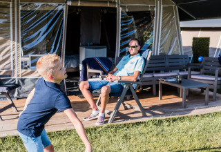 Ragazzo gioca a badminton sull’erba davanti a una lodge di lusso mentre un uomo si rilassa in veranda.