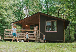 Gezin speelt voetbal voor houten lodge in een bosrijk vakantiepark, Beerze Bulten in Overijssel, Nederland.