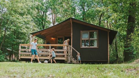 Gezin speelt voetbal voor houten lodge in een bosrijk vakantiepark, Beerze Bulten in Overijssel, Nederland.