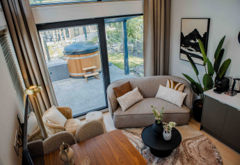 Salon de lodge moderne avec grandes fenêtres, canapés confortables, déco élégante et jacuzzi extérieur.