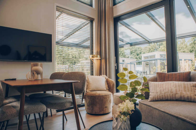 Modern lodge living room with large windows, dining area, gray sofa, TV, and view of terrace and trees.