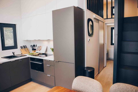 Modern lodge kitchen with grey cabinets, white overhead cupboards, and a black staircase to a loft.
