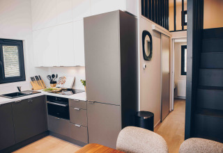 Cucina moderna di lodge con mobili grigi, pensili bianchi e scala nera che porta a un soppalco.