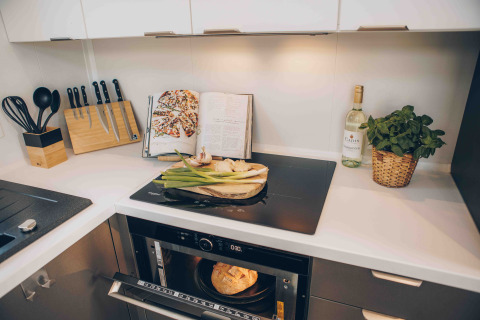 Cucina moderna in un lodge con piano cottura, set di coltelli, ricettario, vino, erbe e pane nel forno.