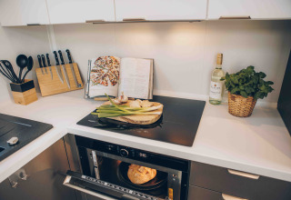Moderne lodge-keuken met inductiekookplaat, messenblok, open recept, witte wijn en ovenvers brood.