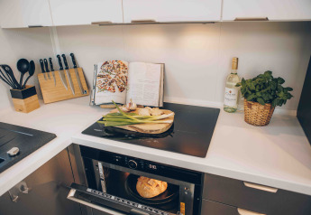 Moderne Küche in einer Lodge mit Herdplatte, Messerblock, Kochbuch, Weißwein, frischen Kräutern und Brot im Ofen.