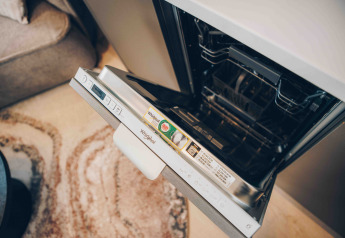 Geöffnete Whirlpool-Geschirrspülmaschine in einer gemütlichen Lodge mit Teppich und Sofa im Hintergrund.