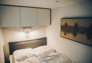Moderne soveværelse i en lodge med grå hovedgærde, hvidt sengetøj, vægkunst og loftskabe.