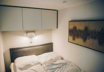 Moderne soveværelse i en lodge med grå hovedgærde, hvidt sengetøj, vægkunst og loftskabe.