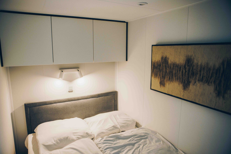 Dormitorio moderno en una cabaña, cabecero gris, ropa de cama blanca, arte mural y armarios arriba.