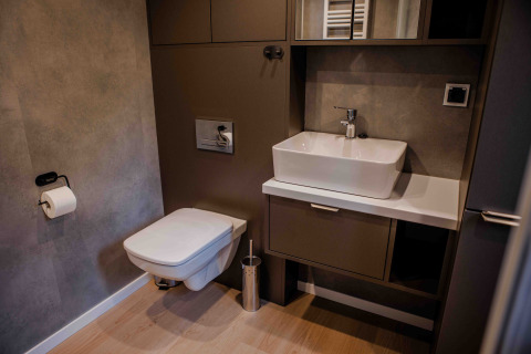 Baño moderno en un lodge con inodoro suspendido, lavabo rectangular y suelo con apariencia de madera.