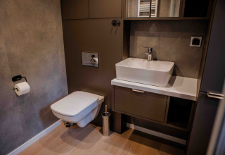 Modernes Badezimmer in einer Lodge mit wandmontiertem WC, eckigem Waschbecken und Holzfußboden.