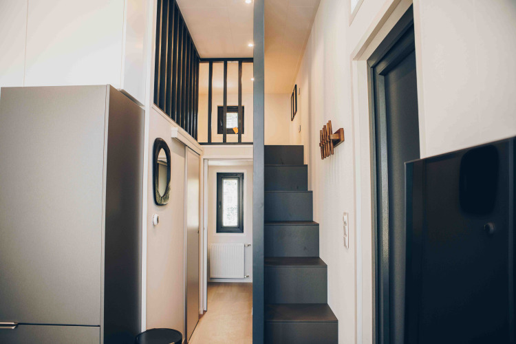 Vue intérieure d’un lodge moderne avec un escalier étroit, une mezzanine et un design minimaliste en tons neutres.