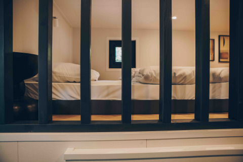 Vista a través de barrotes negros hacia un dormitorio de lodge con cama grande y ambiente cálido.