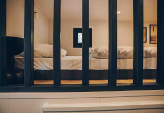 View through black bars into a cozy lodge bedroom featuring a neatly made bed and soft lighting.