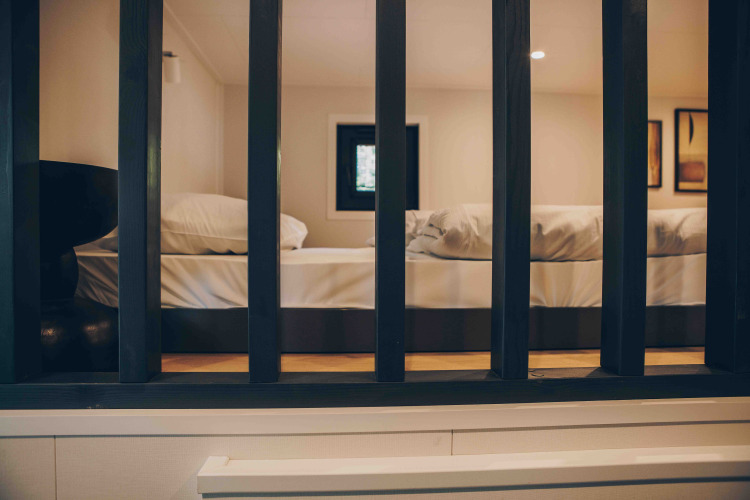 Blick durch schwarze Gitter in ein gemütliches Lodge-Zimmer mit einem großen Bett und Kissen.