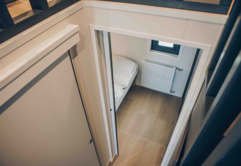 Blick von oben auf ein kleines Schlafzimmer mit Holzboden, Bett und Heizung in einer modernen Lodge.