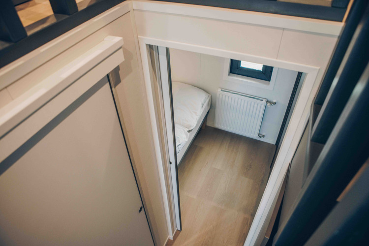 Vista aérea de un dormitorio pequeño con piso de madera, radiador y cama en una acogedora cabaña.