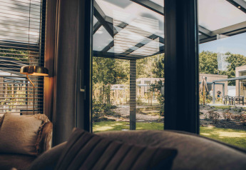 Blick aus einer Lodge mit großen Fenstern auf einen modernen Gartenbereich und benachbarte Lodges.