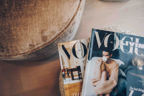 Two magazines, including Vogue, rest on a soft table next to a chair in a cozy lodge interior.