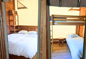 Zwei getrennte Schlafzimmer in einem Safari-Zelt mit Holzwänden, Doppelbett links, Etagenbett rechts.