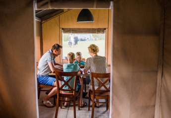 Een familie zit samen rond een tafel in een safaritent en brengt gezellige tijd in de natuur door.