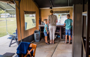Eine Familie bereitet Essen in einer Safari-Zeltküche zu, mit Blick auf den Campingplatz draußen.