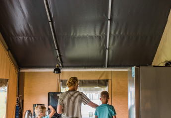 Madre e due bambini che cucinano insieme in una cucina dentro una tenda safari, atmosfera da campeggio.