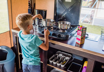 Ragazzo cucina su un fornello a gas in una tenda safari, con pentole, succo e utensili da cucina.