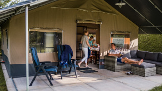 Famille se détend et profite de la terrasse devant une tente safari de luxe aménagée confortablement.