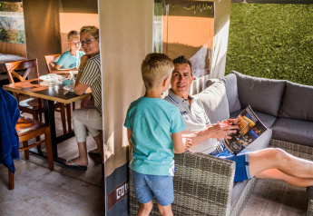 Eine Familie verbringt gemeinsam Zeit in einem Safarizelt mit Essbereich und Lounge, umgeben von Natur.