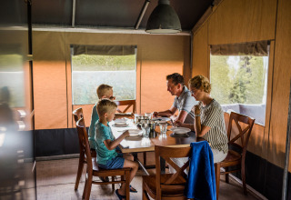 Eine vierköpfige Familie isst gemeinsam an einem Tisch in einem gemütlichen Safarizelt mit Naturblick.