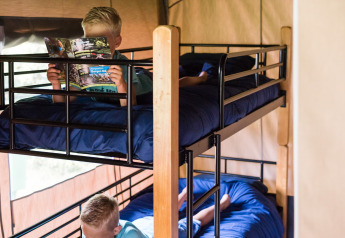 Due bambini leggono libri su un letto a castello con lenzuola blu in una tenda safari beige.