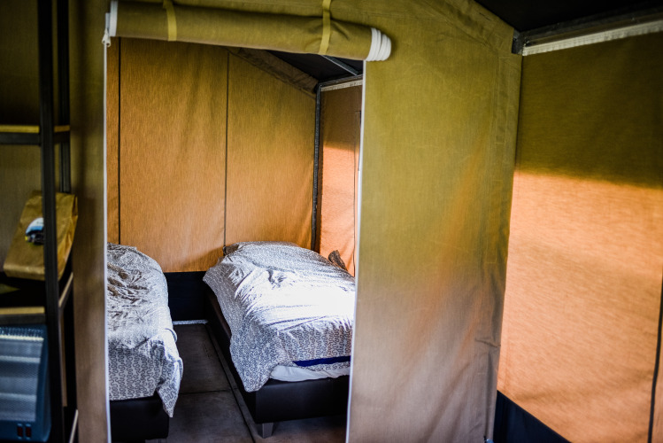 Vista interior de una tienda safari con dos camas individuales y ropa de cama bajo luz natural.
