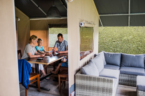 Una famiglia è seduta a un tavolo all’interno di una tenda safari, con un divano e vista naturale.