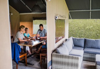 Eine Familie sitzt gemeinsam an einem Tisch in einem komfortablen Safarizelt mit Sofa und Tageslicht.