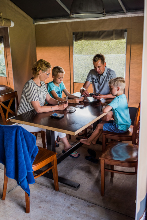 Una famiglia gioca a carte seduta a un tavolo all'interno di una tenda safari, atmosfera rilassata.