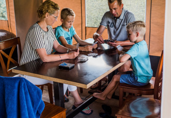 Een familie speelt kaartspel aan een tafel in een safaritent, gezellige en ontspannen sfeer.