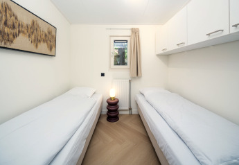 Luminoso cuarto de alojamiento con dos camas individuales, ventana, armarios, lámpara y cuadro decorativo.