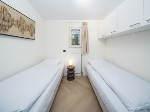Bright lodge room featuring two single beds, window, overhead cabinets, bedside lamp, and wall art.