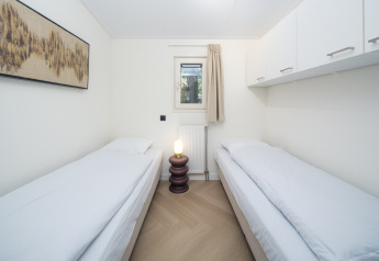 Chambre lumineuse en lodge avec deux lits simples, fenêtre, placards en hauteur, lampe et tableau mural.