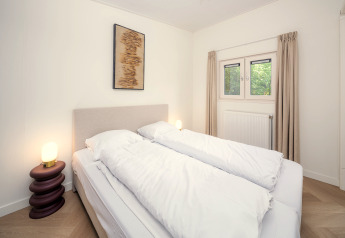 Dormitorio luminoso en una cabaña con cama doble, lámparas, obra de arte en la pared y ventana con cortinas.