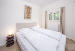 Dormitorio luminoso en una cabaña con cama doble, lámparas, obra de arte en la pared y ventana con cortinas.