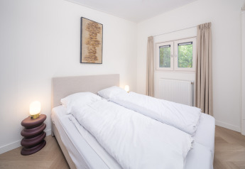Chambre lumineuse et épurée d’un lodge avec lit double, lampes, tableau mural et fenêtre avec rideaux beiges.