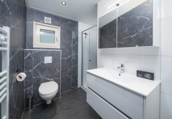 Bagno moderno in un lodge con piastrelle effetto marmo scuro, wc sospeso, doccia e grande specchio.