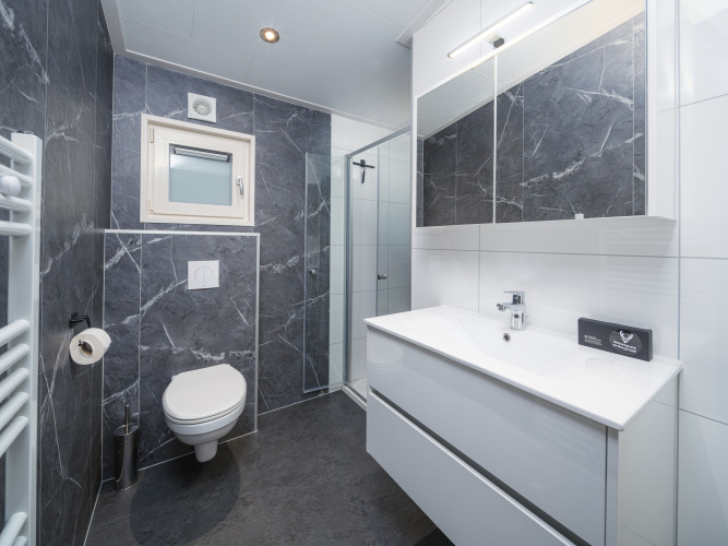 Modernes Lodge-Badezimmer mit dunklen Marmorfliesen, Wandtoilette, Dusche und großem Spiegel.