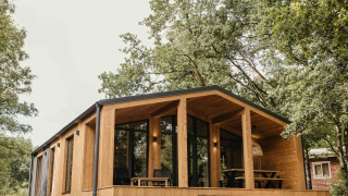 Moderne houten Hill Top Scandi met Sauna-hut met groot terras, gelegen tussen groene bomen.