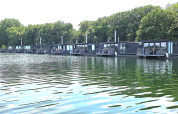 Mehrere moderne Hausboote schwimmen auf einem ruhigen See, umgeben von grünen Bäumen und Natur.