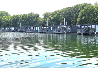 Varios modernos barcos-casa flotan en un lago tranquilo, rodeados de frondosos árboles verdes y naturaleza.