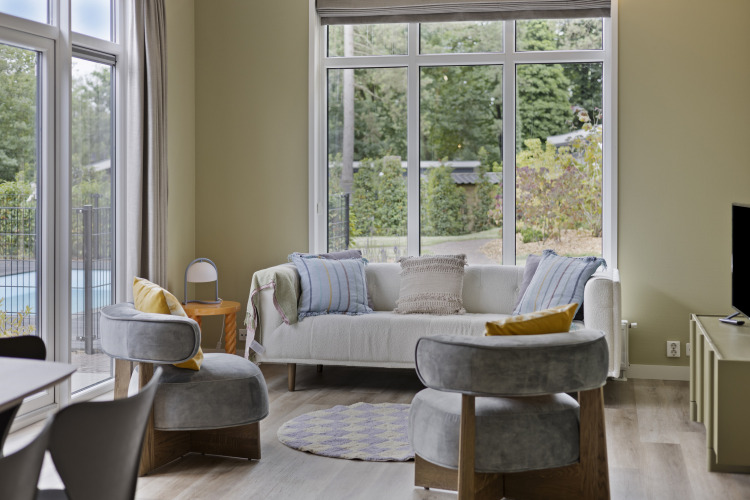 Helles Wohnzimmer mit großen Fenstern, modernem Sofa und Blick auf den Garten im De Thijmse Berg Lodge.
